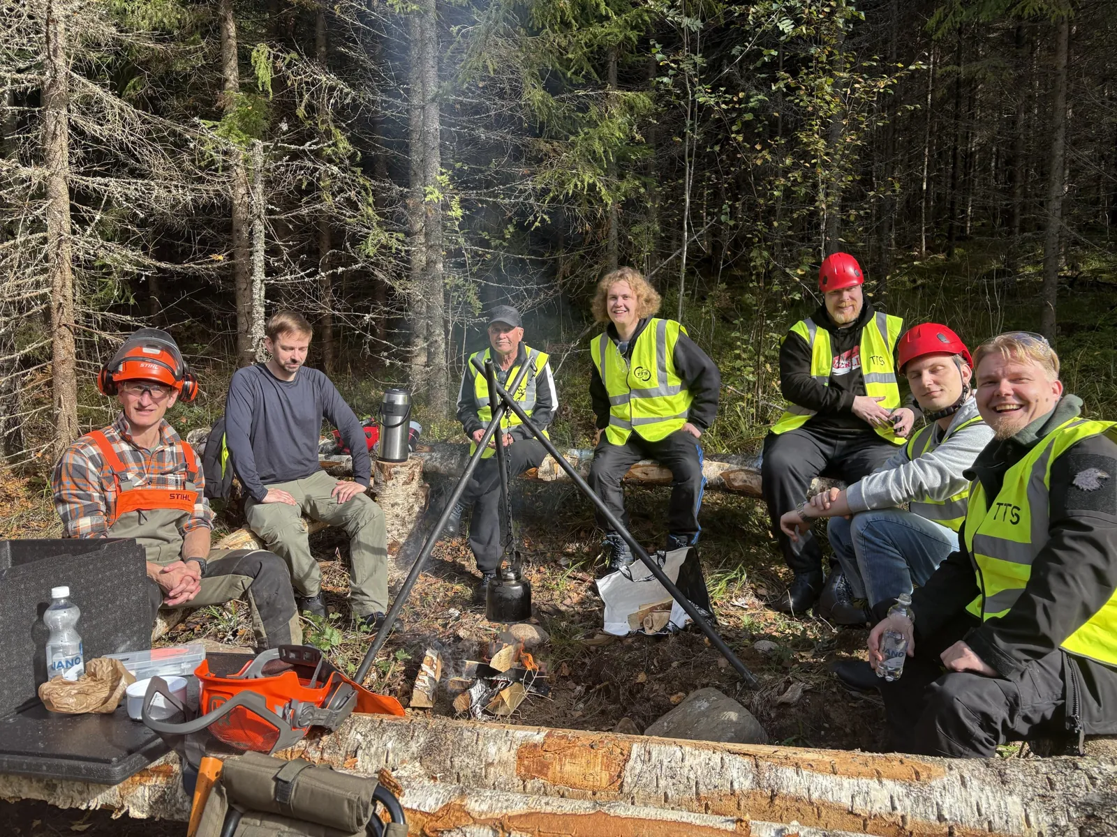 Ryhmäkuva nuotion ympärillä metsässä.